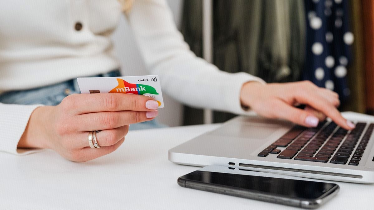 Hands holding a debit card over a laptop keyboard at the moment a download asks for payment