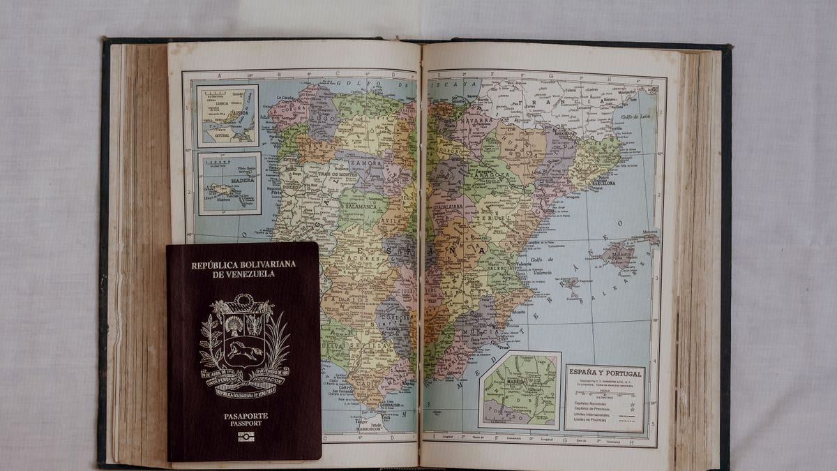 A passport rests atop an open vintage atlas showing a detailed map of Spain and Portugal.