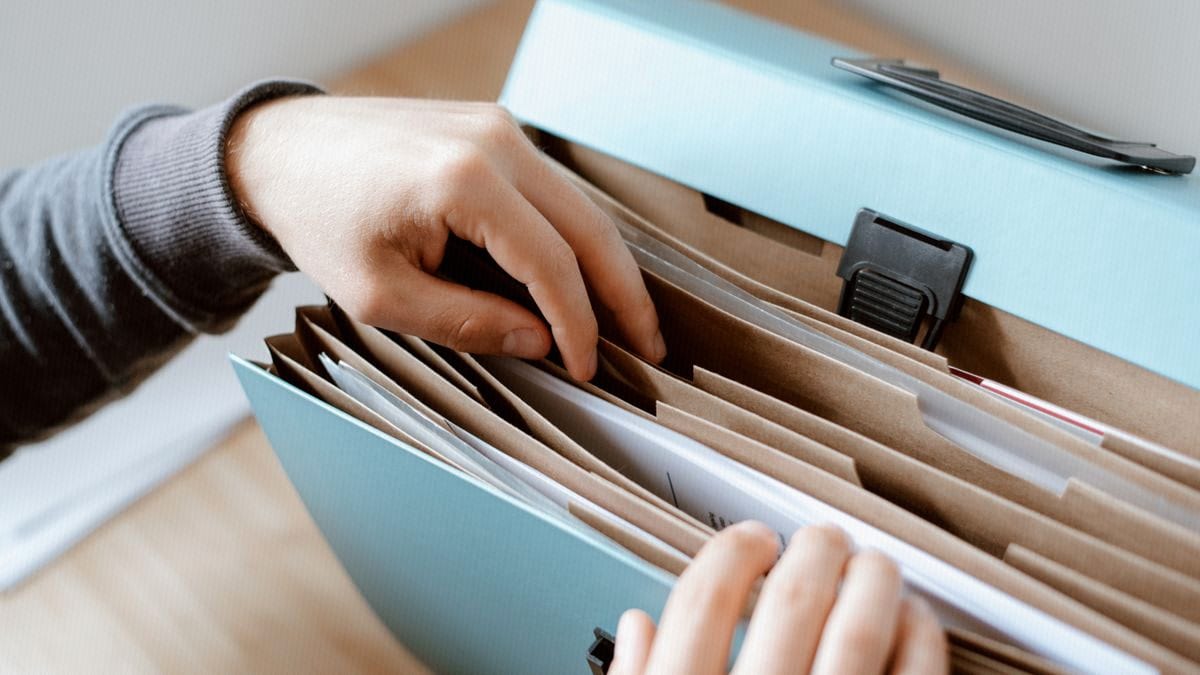 Hands sort through the labeled sections of an accordion file organizer, grouping loose documents into order.