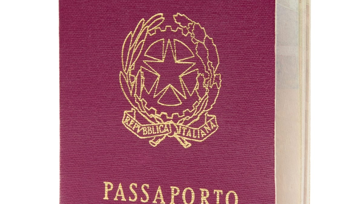 An Italian passport stands upright against a plain white background, its cover embossed in gold.