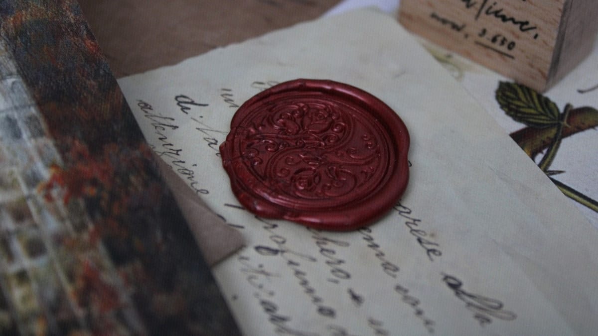 A dark red wax seal presses down on a handwritten letter beside a wooden stamp.